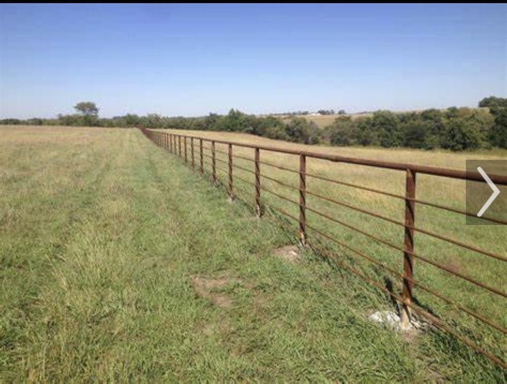 Rusty metal fence running through a grassy field under a clear blue sky.