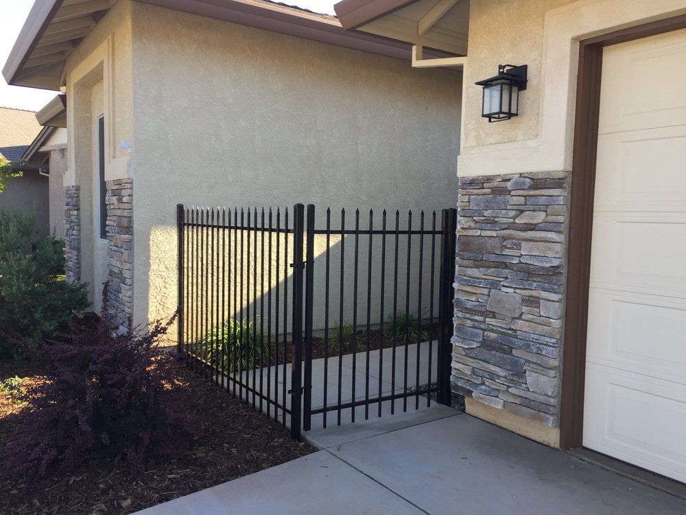 Black metal gate beside a stucco house and garage with stone siding