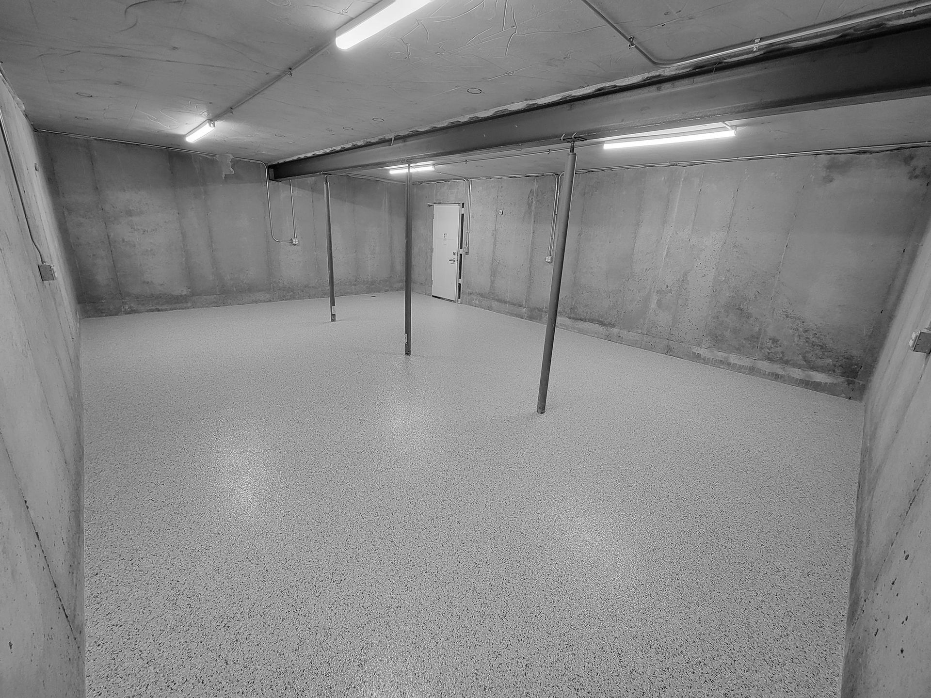 A black and white photo of an empty basement with a concrete floor.
