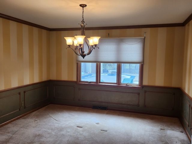 Room before it has been painted. The room has yellow-striped wallpaper and brown baseboards.