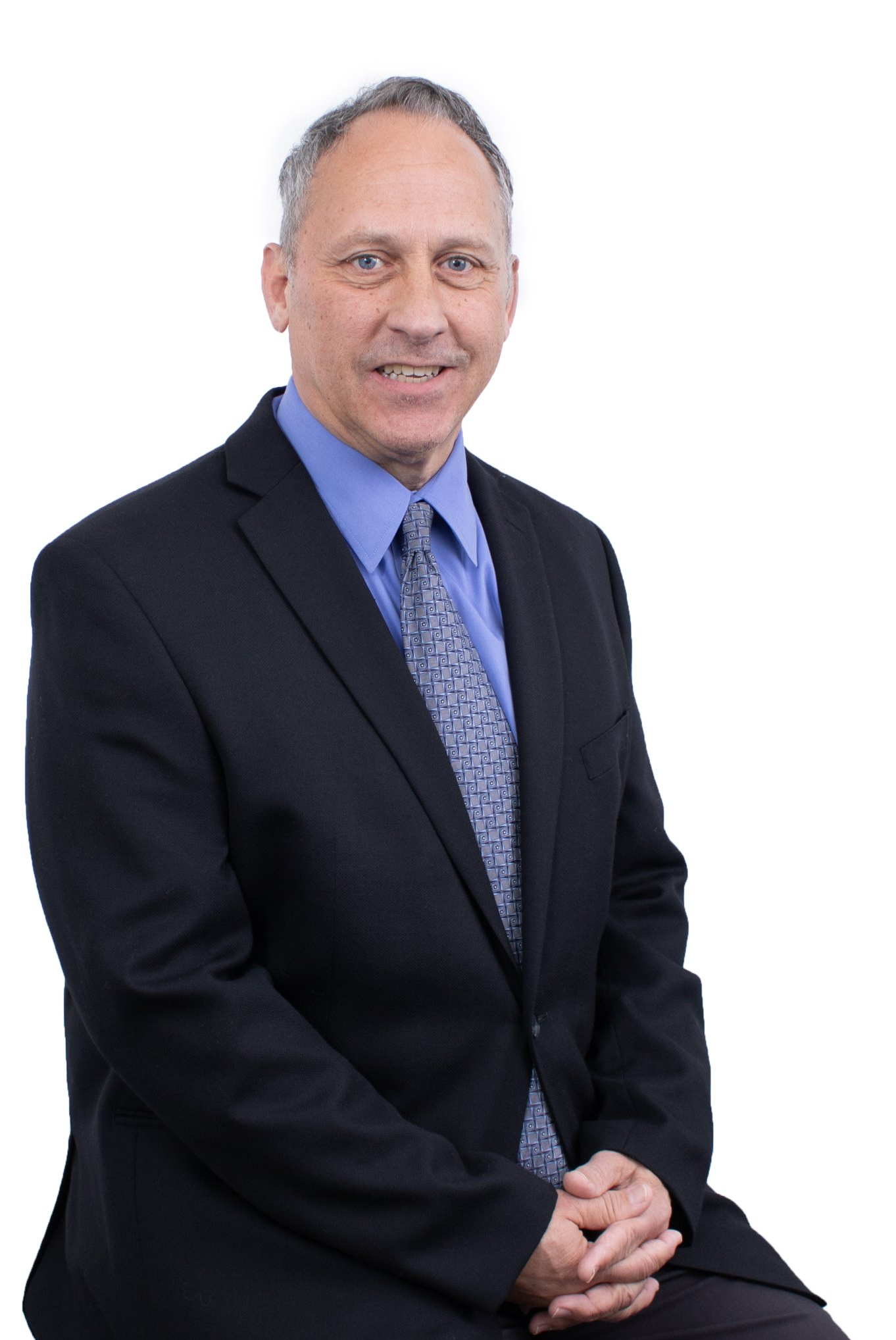 Man in suit seated, smiling, blue shirt and patterned tie.