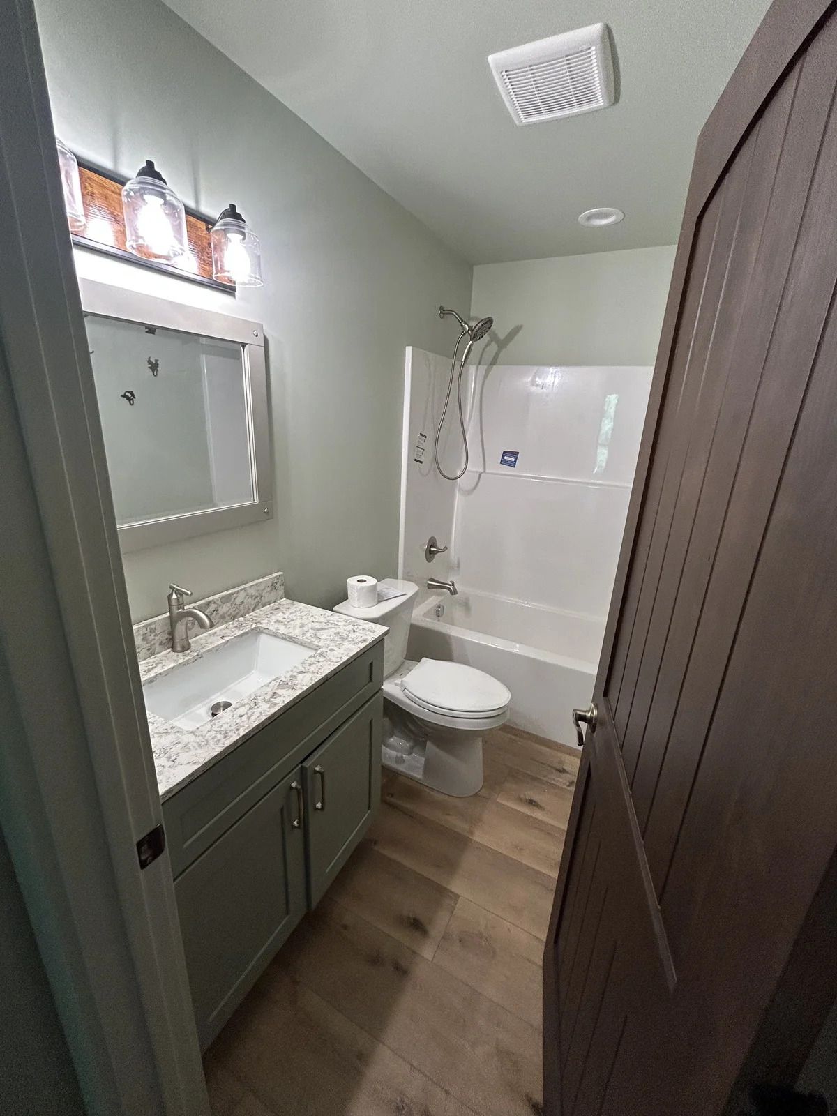 A modern bathroom featuring a grey vanity with a speckled countertop, a toilet, and a white tub-shower combination.