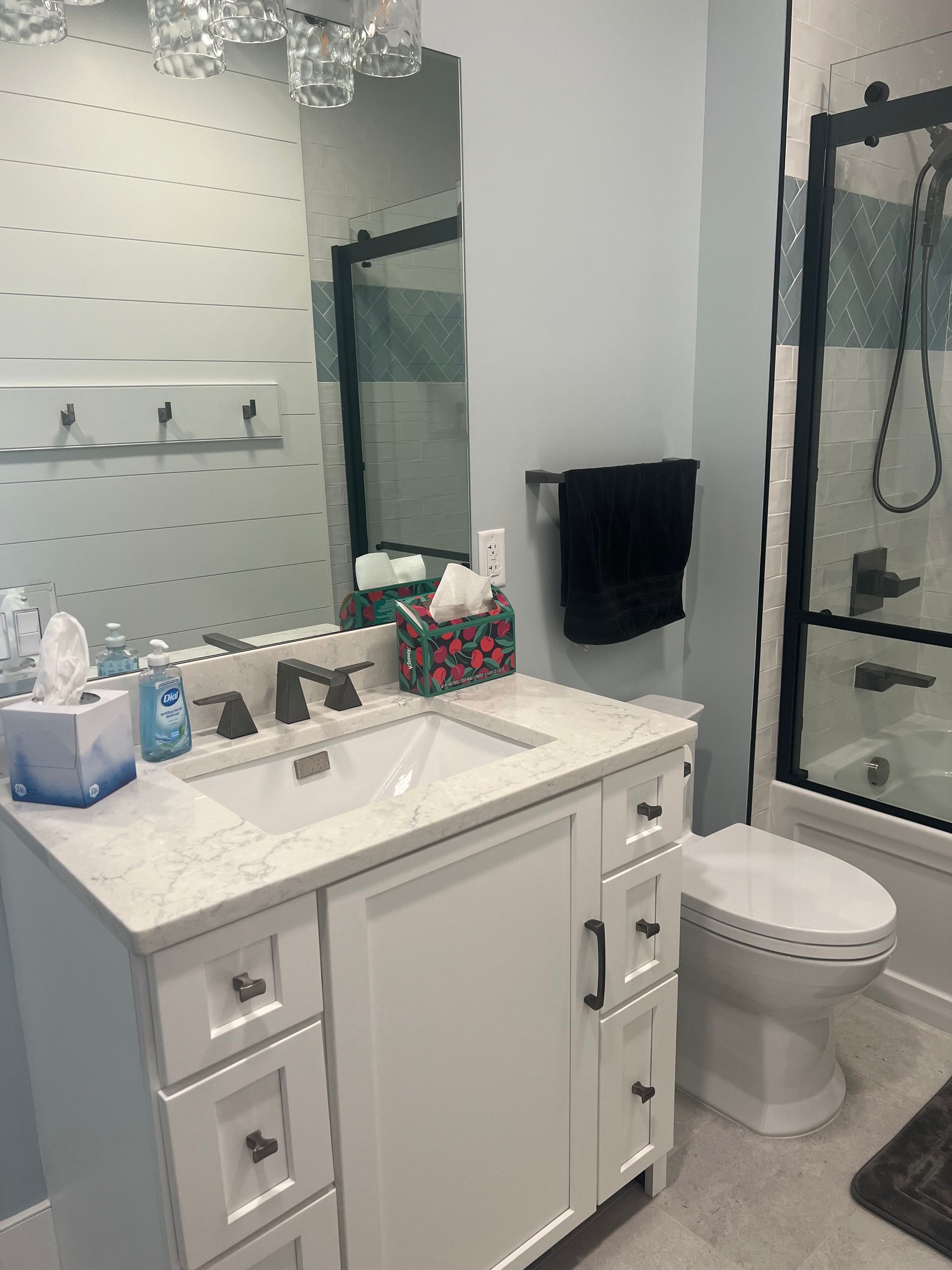 A modern bathroom with a white vanity, marble countertop, large mirror, and a black-framed walk-in shower.