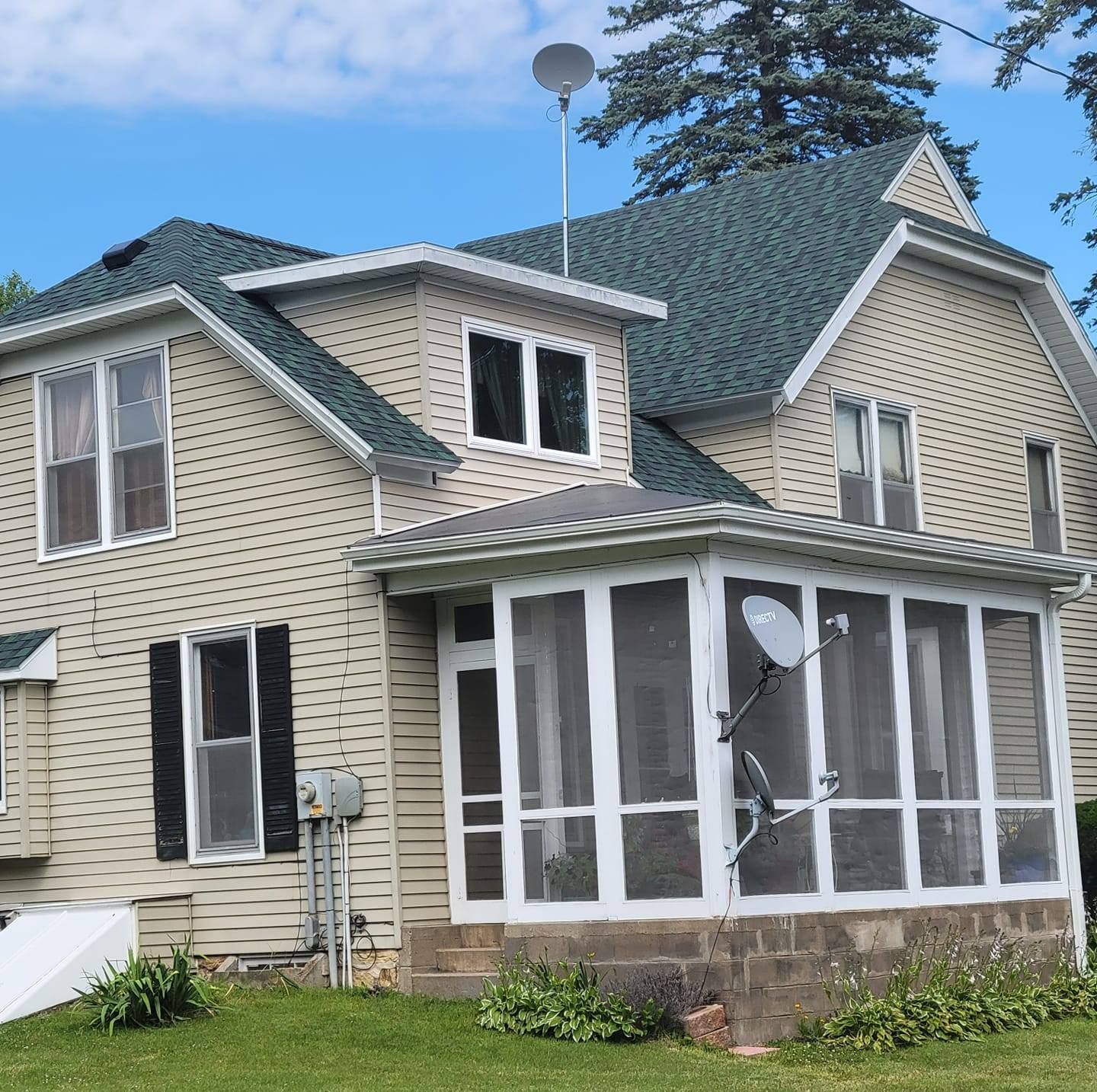 Beige two-story house with white trim, enclosed porch, and satellite dish under a blue sky.