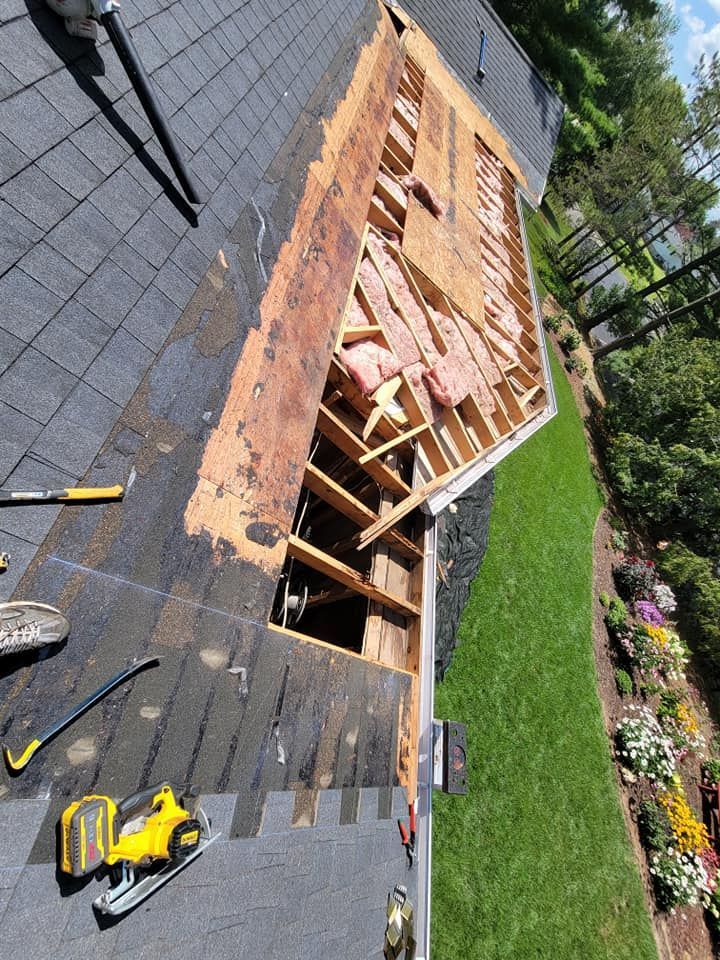Roof under repair with exposed wooden framing, black shingles, and tools on a sloped rooftop.