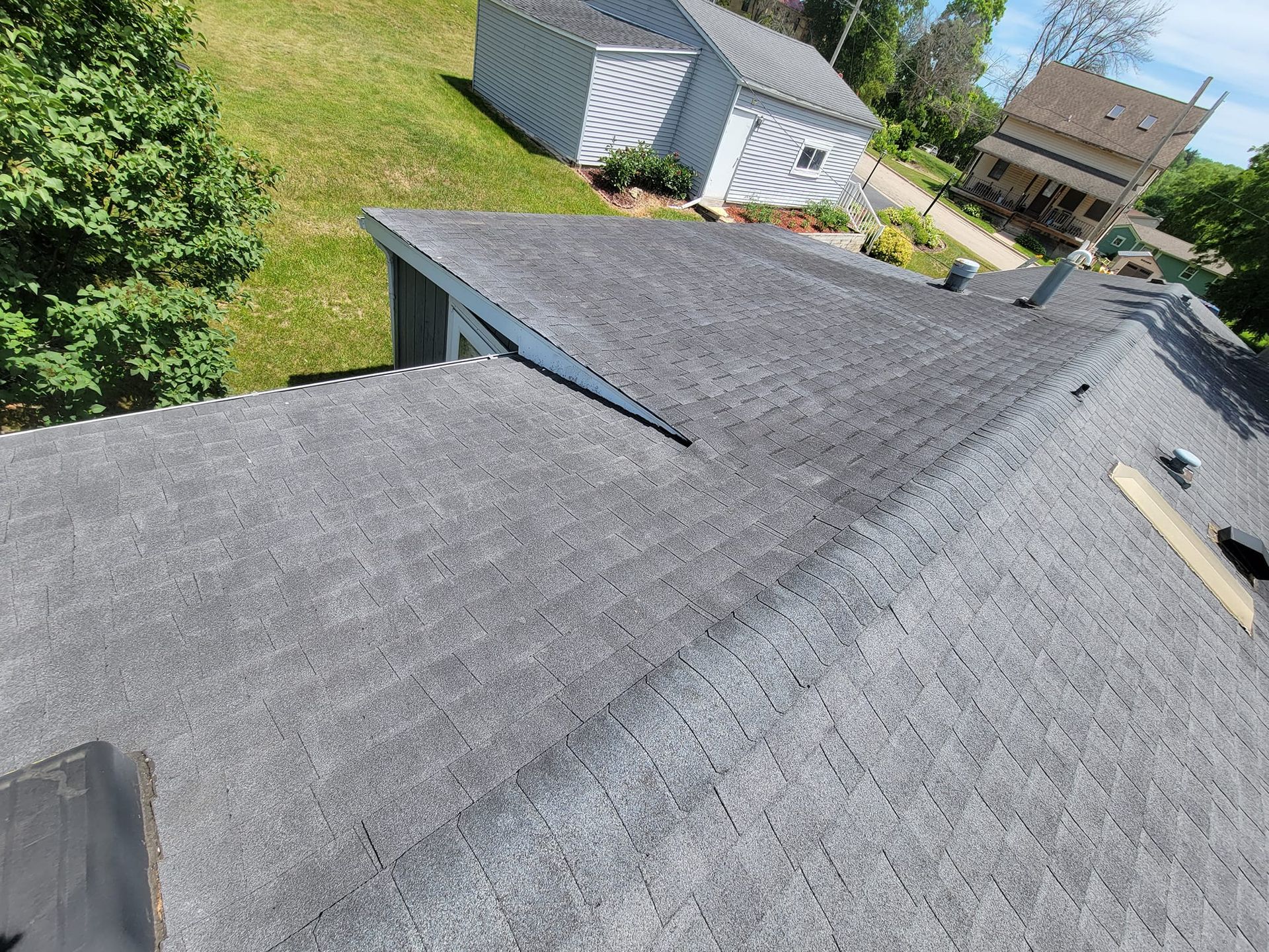 Gray shingled rooftop with a small roof vent, overlooking a green backyard and neighboring house