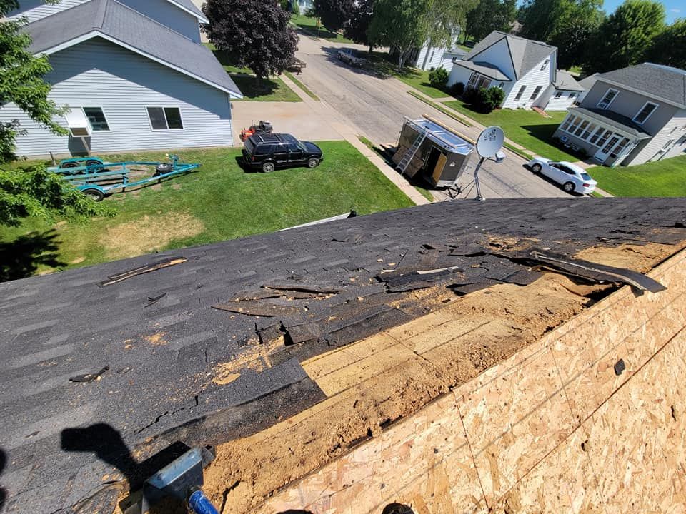 Rooftop with damaged shingles overlooking a suburban neighborhood and street below