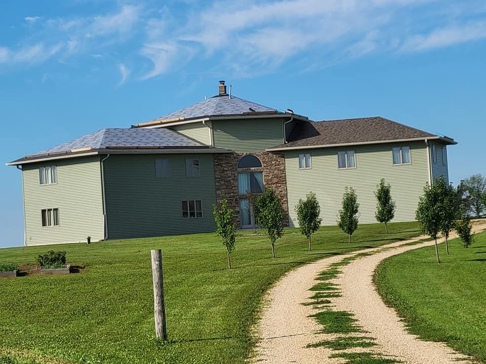 Green house with a round roof on a grassy hill, with a curving dirt path under a blue sky