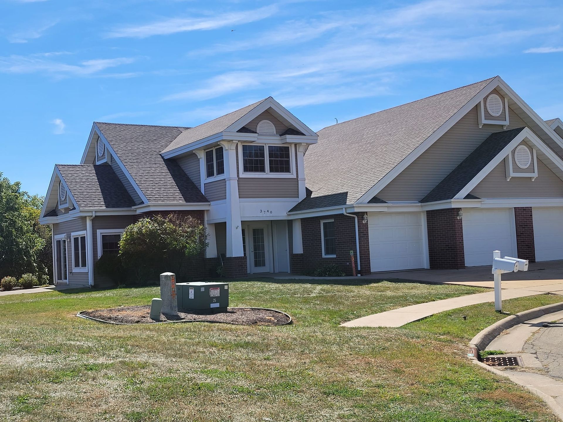 Suburban house with beige siding, gabled roof, garage, and front lawn under a blue sky