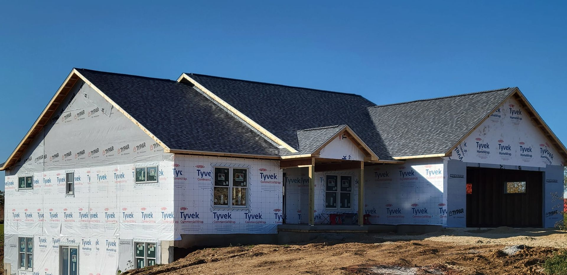 New house under construction with white siding, dark roof, and attached garage under a blue sky