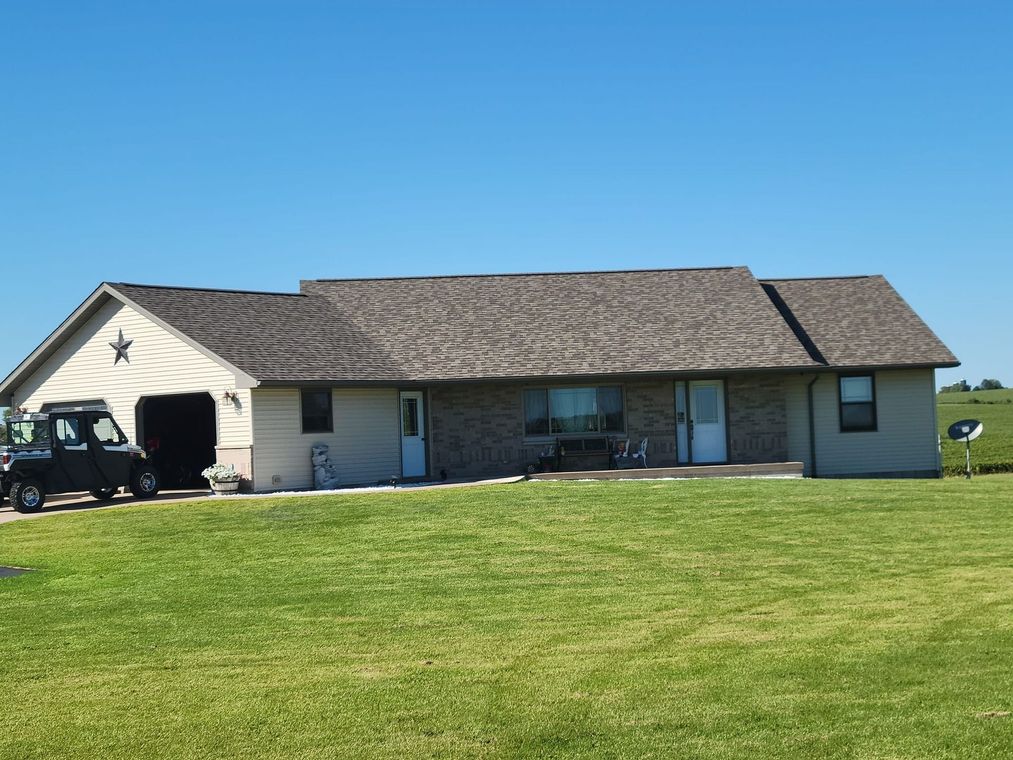 Single-story beige house with a shingled roof and large green lawn under a clear blue sky.
