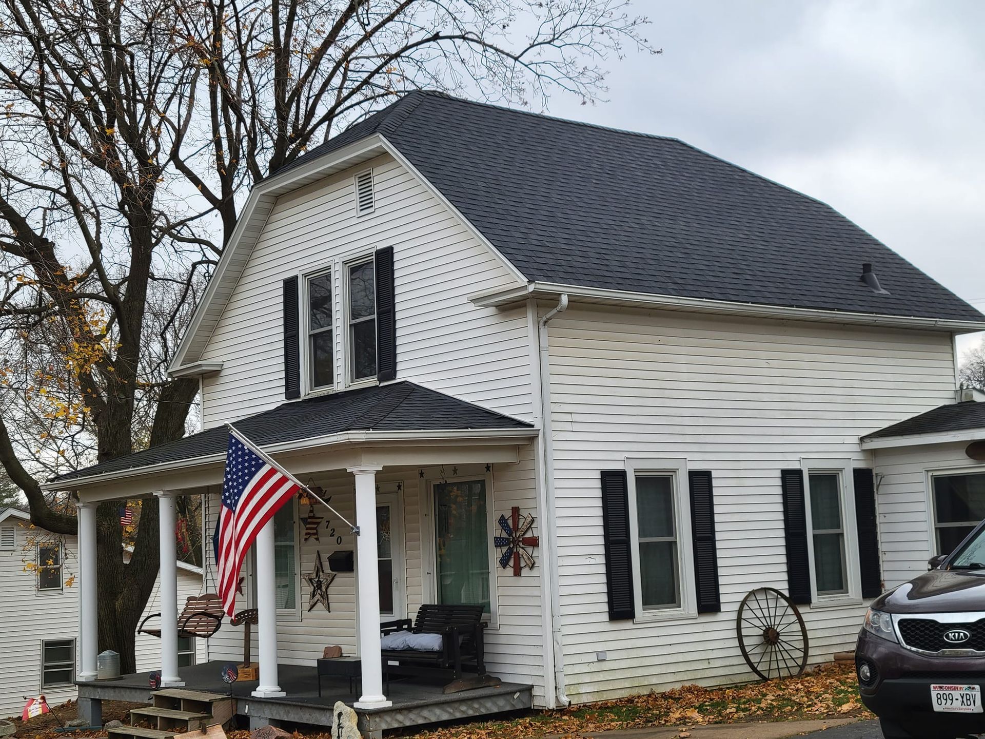 White house with black shutters and an American flag on the porch, viewed from the front.
