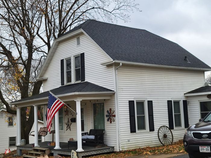 White house with black shutters and an American flag on the porch, viewed from the front.