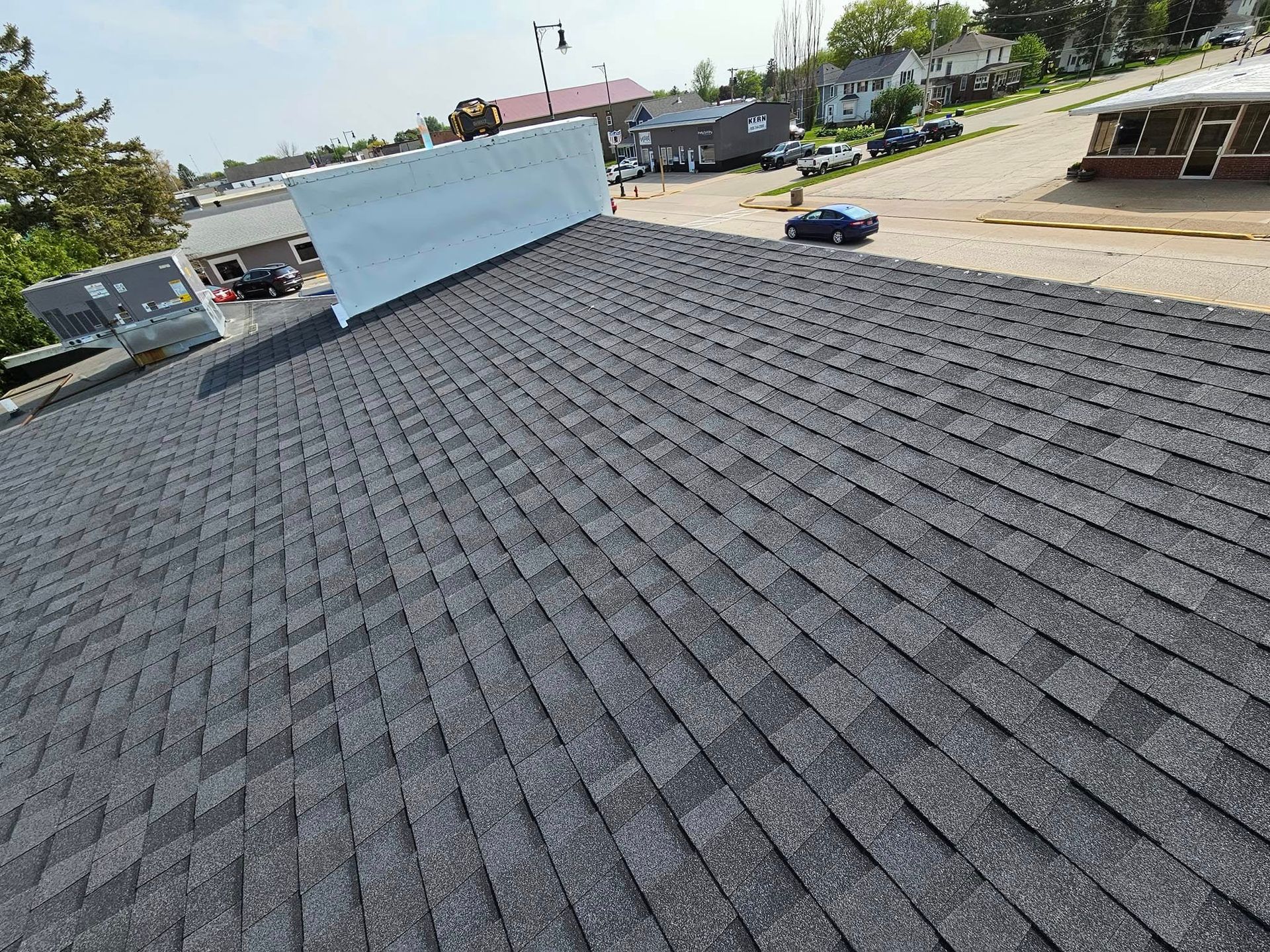 View from a rooftop with dark gray shingles and a light blue wall, overlooking a street and buildings.