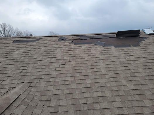 Damaged shingle roof with missing sections and exposed underlayment under a cloudy sky