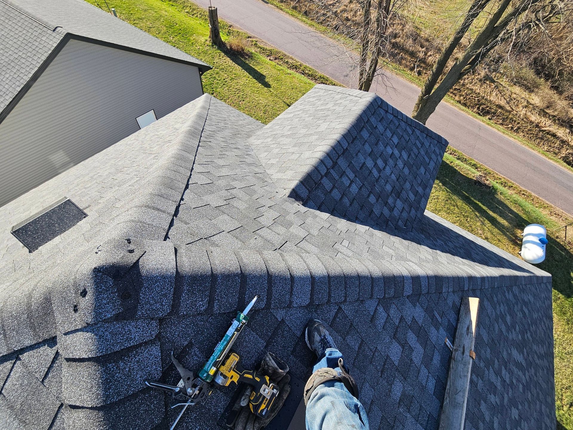 Roof inspection with two workers on a gray shingled roof near a road and trees