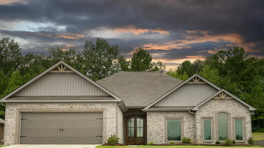 Suburban brick house with two-car garage under a cloudy sunset sky