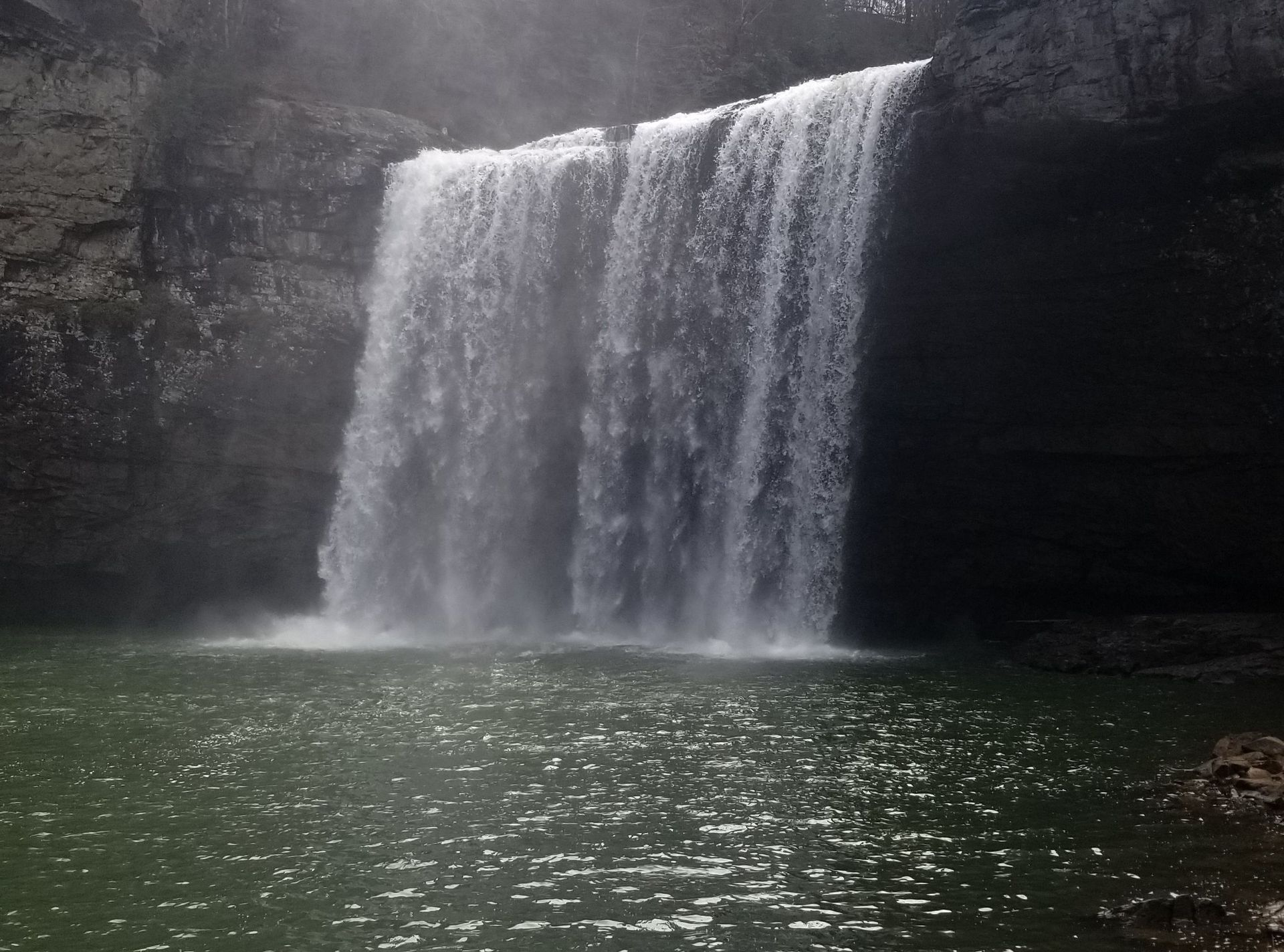 Waterfall cascading into a dark, rocky pool with mist rising at the base.