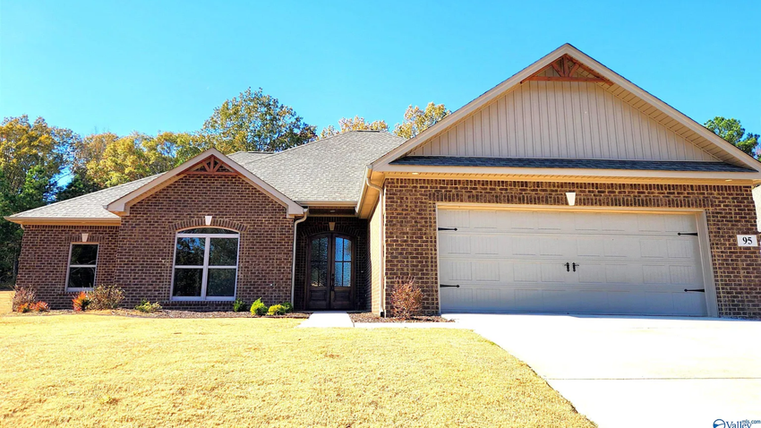 Single-story brick house with a white garage door and gabled roof in bright sunlight