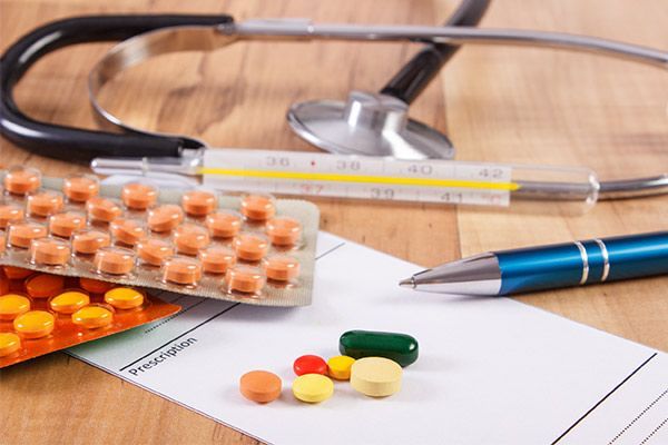 Pills, thermometer, stethoscope, and pen on a paper. Medical equipment on a wooden surface.
