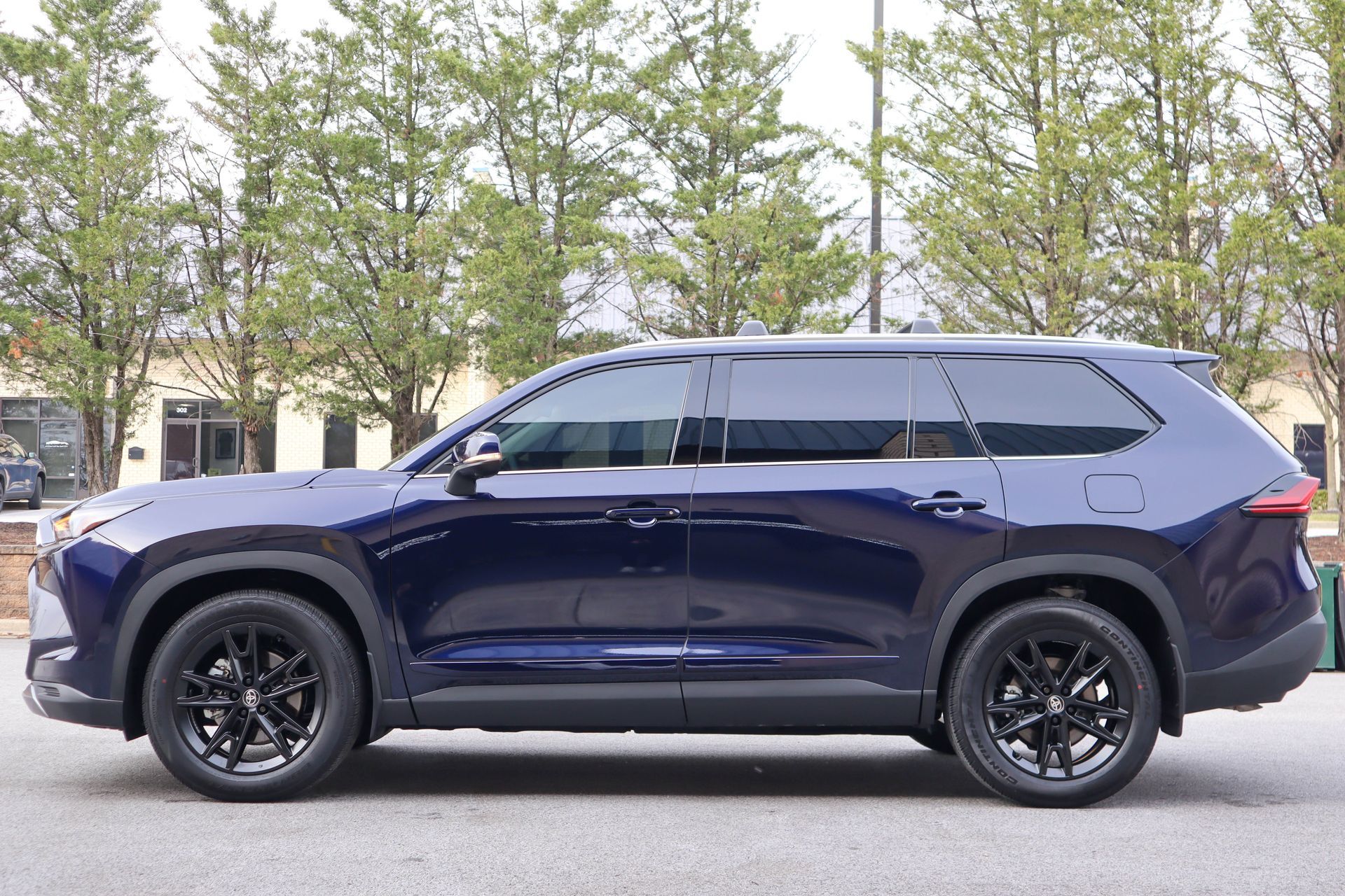 Dark blue SUV with black wheels parked on a street with trees and a building in the background.