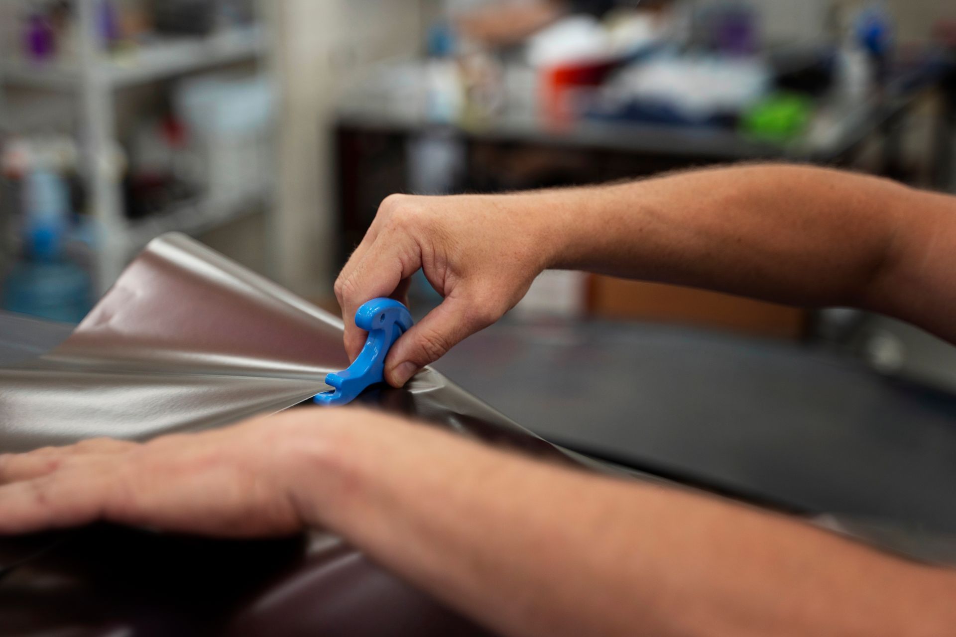 A person is wrapping a car with a blue tool.