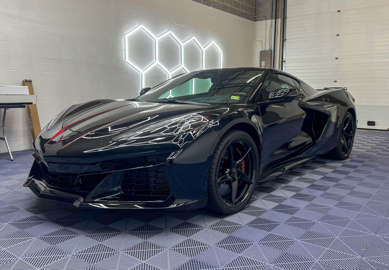 Black Corvette sports car in a showroom with hexagon-shaped lights and tile floor.