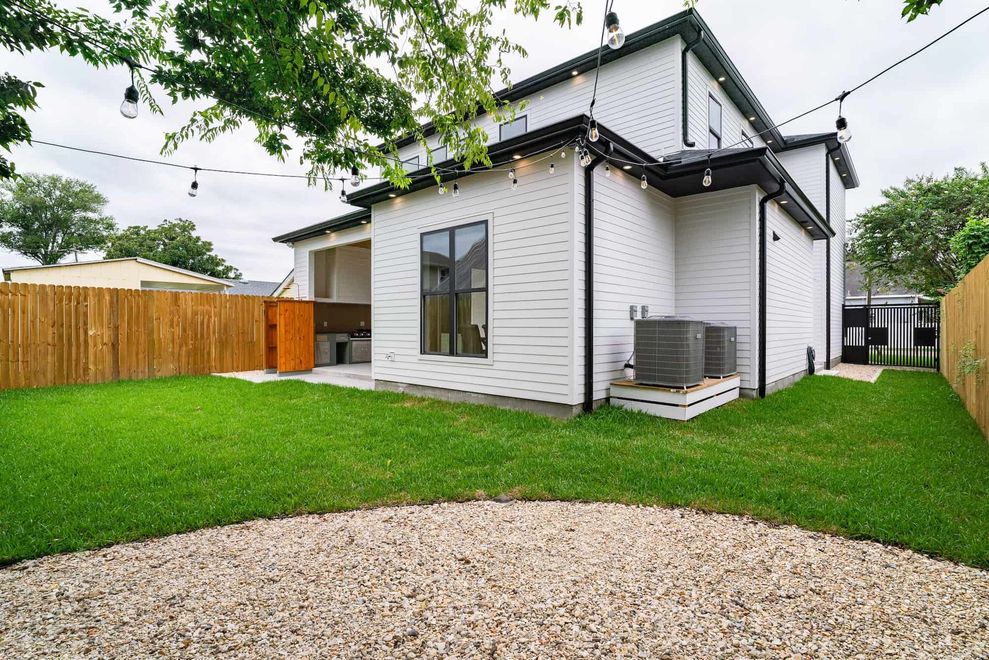 Modern white house with black trim, green lawn, wooden fence, and gravel path in front yard