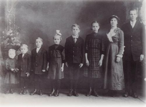 A family of seven poses for a formal portrait. Children stand in front of a woman and a man.
