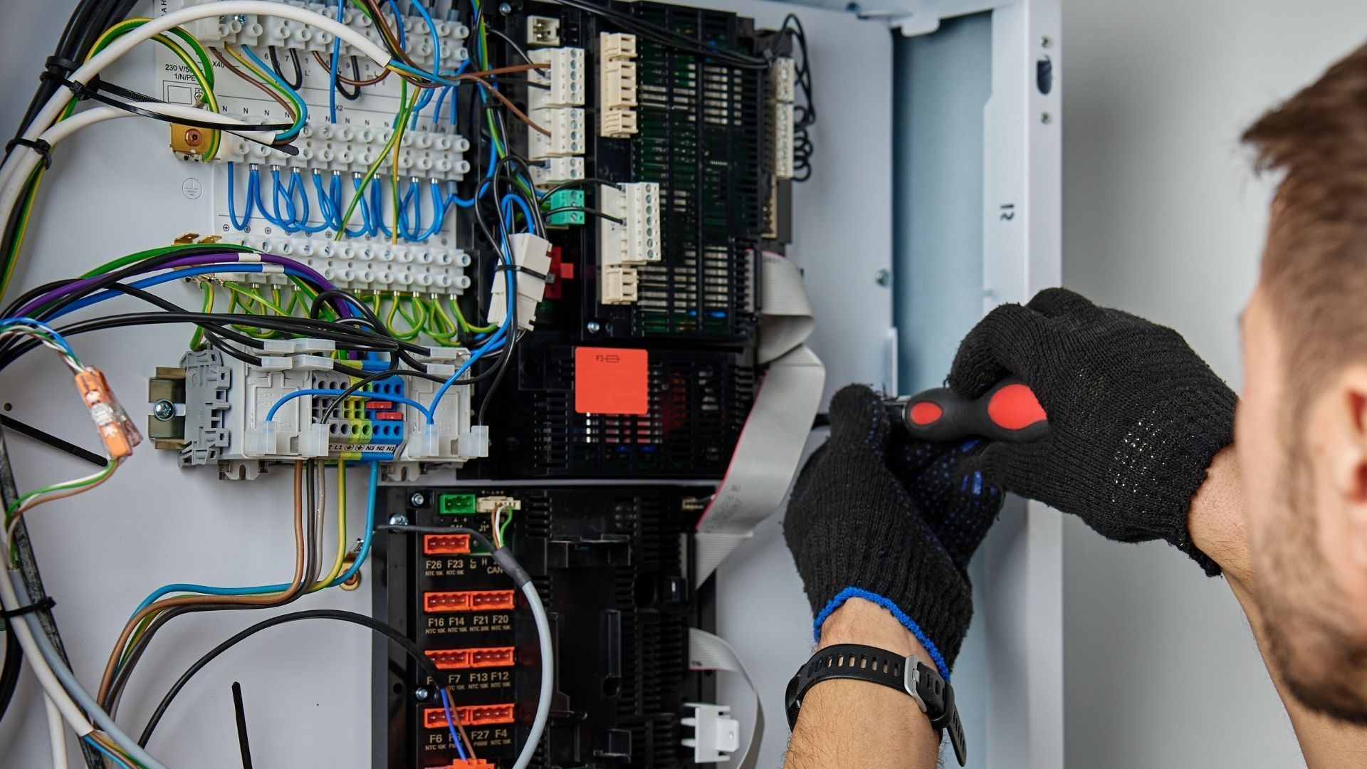 Person using a multimeter to test electrical wiring in a panel.