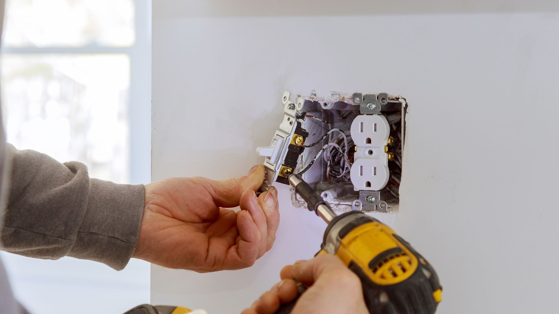 Person using a multimeter to test electrical wiring in a panel.