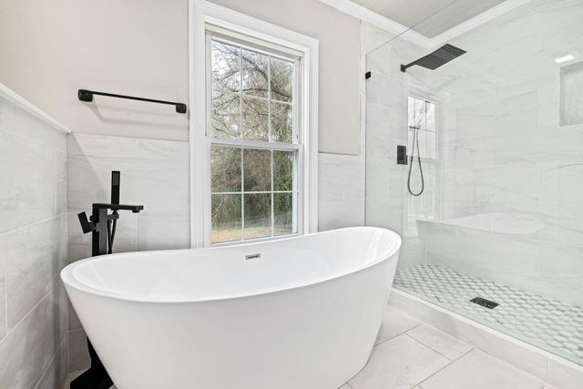 White freestanding bathtub near a window and shower in a modern bathroom.