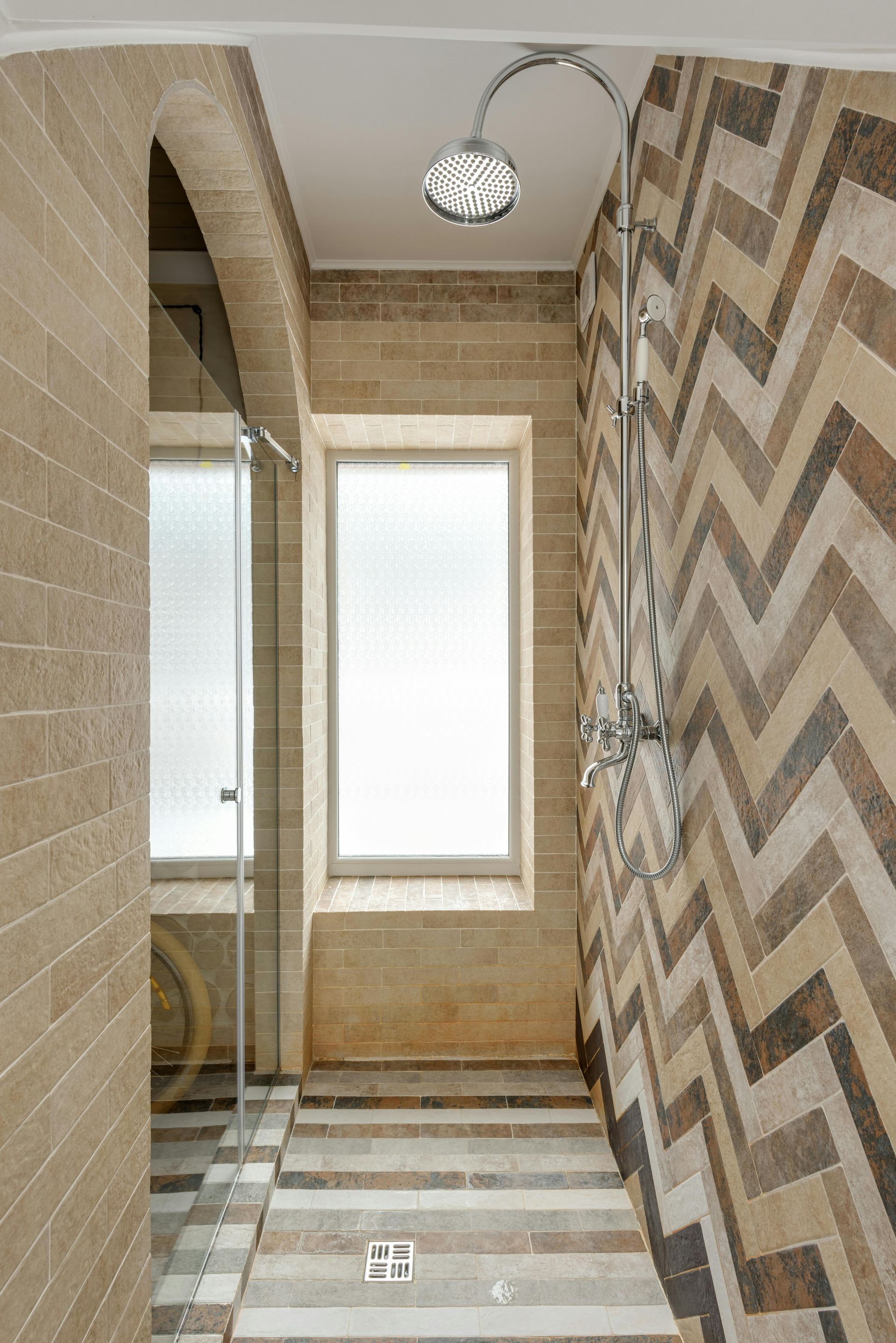 Shower with patterned wall tiles, shower head, window, and glass door.