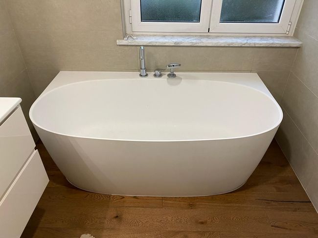 Bagno moderno sui toni del grigio, con lavabo a ciotola bianco, un grande specchio e una vasca da bagno freestanding accanto a una finestra.