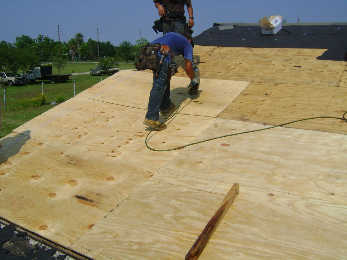 Workers installing plywood roofing on a house roof under construction.