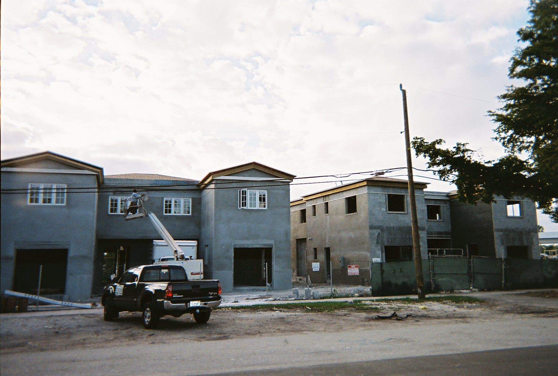 Partially built gray houses on a dirt lot with a pickup truck parked in front