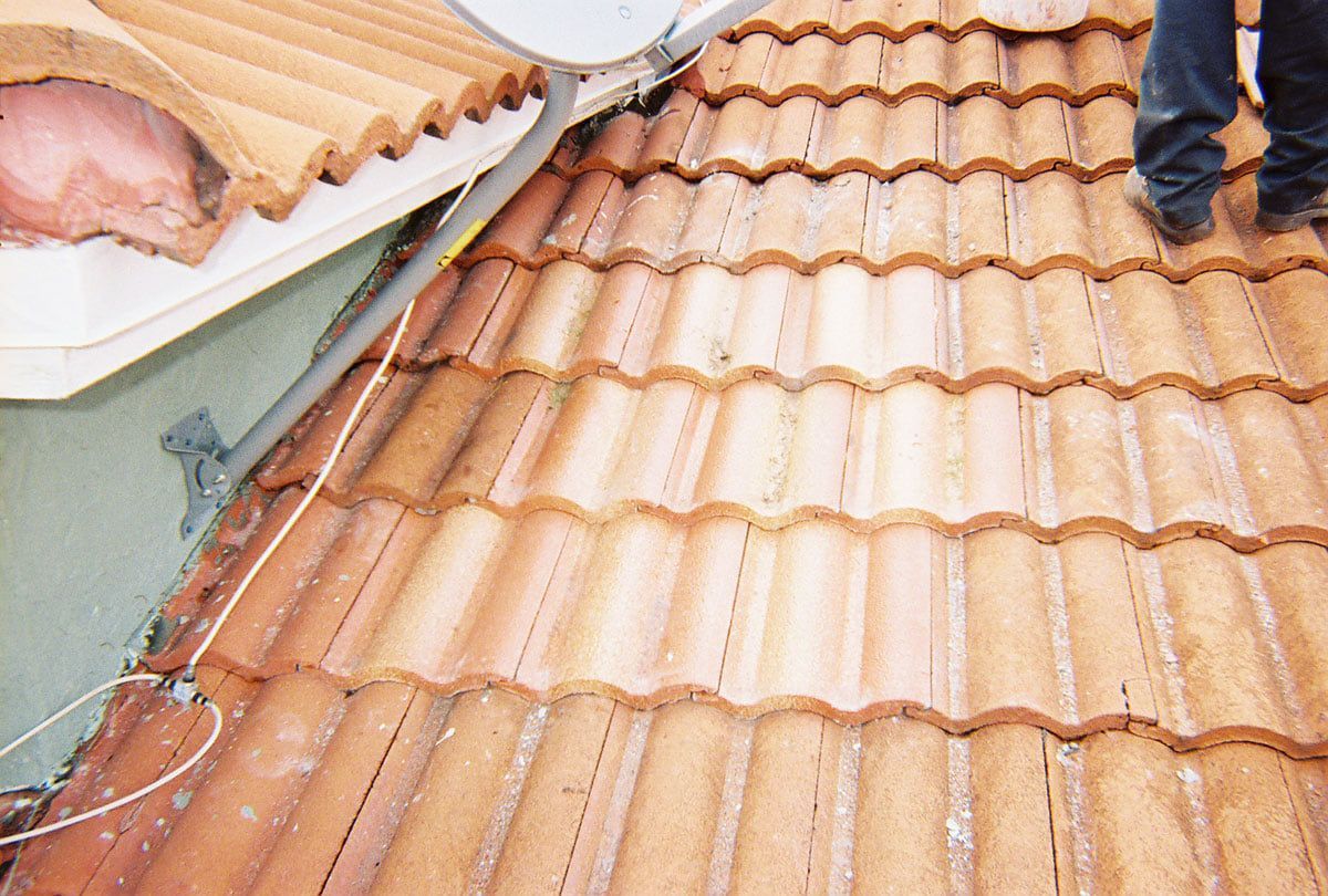 Workers on a terracotta tile roof with tools and building materials nearby