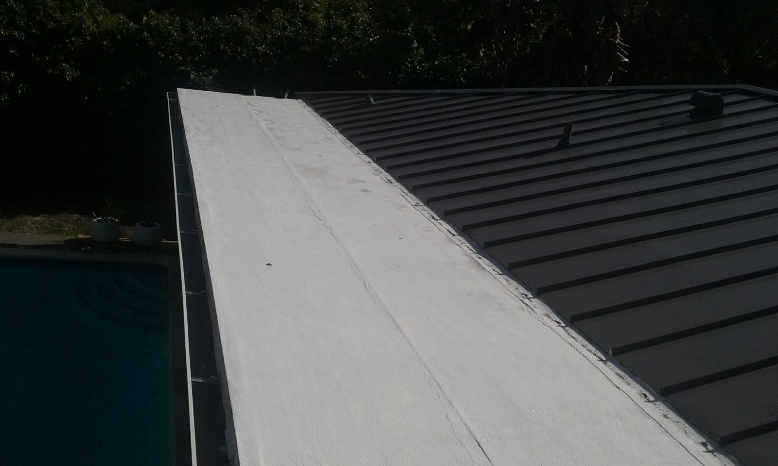 Rooftop with a white parapet beside a dark shingled roof, viewed from above.