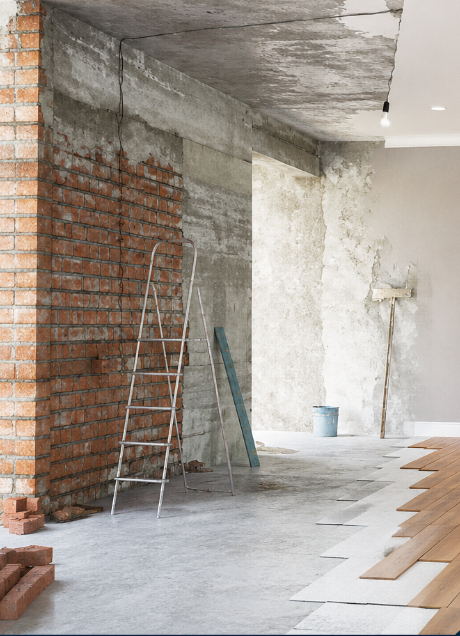 Stanza parzialmente ristrutturata con pareti in mattoni a vista e intonaco, scala e pavimento in legno in fase di installazione.