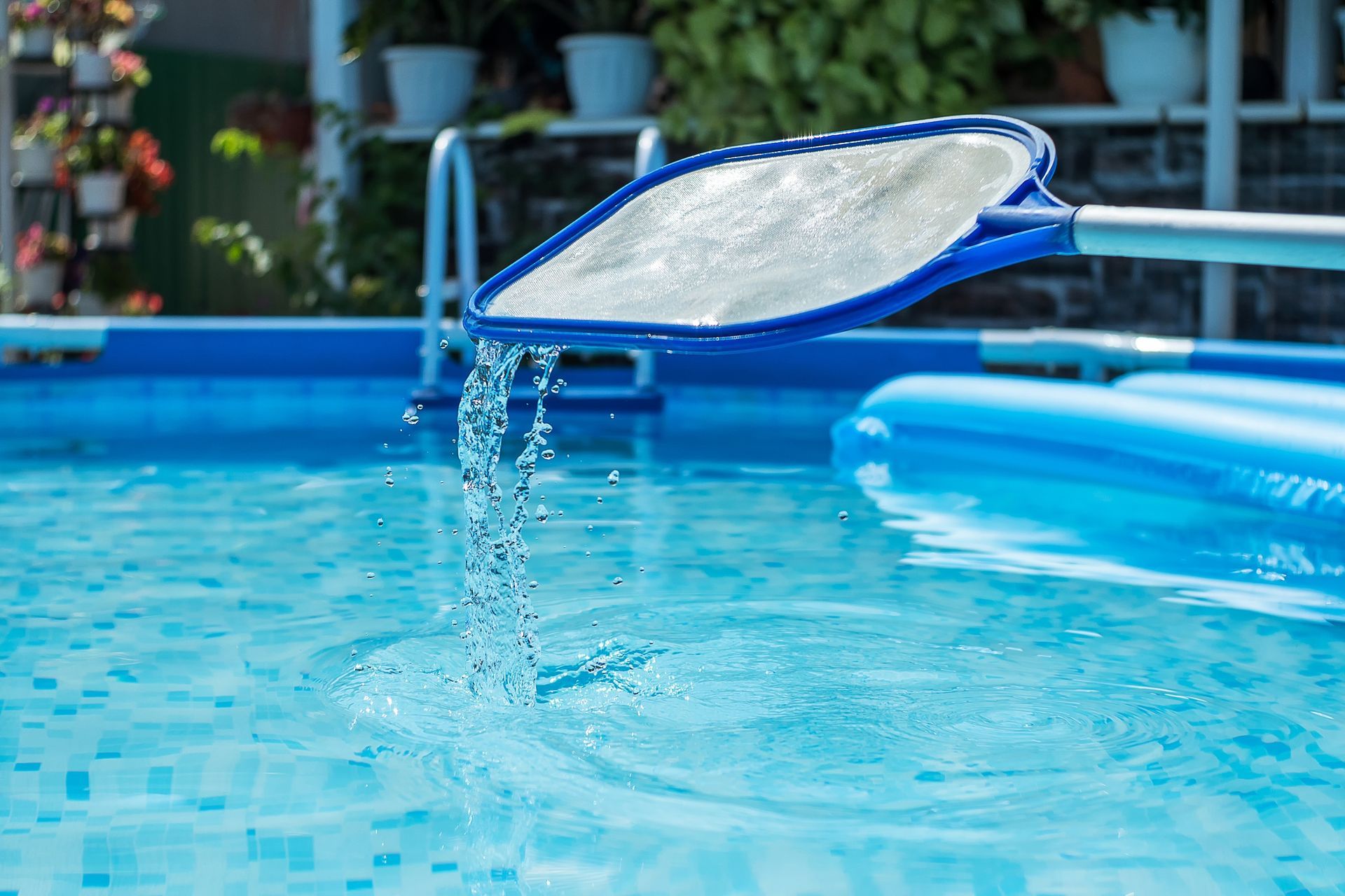 A person using a blue pool net to remove debris from a pool. Water streams out of the net.