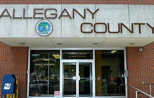 The allegany county office building has a blue mailbox in front of it.