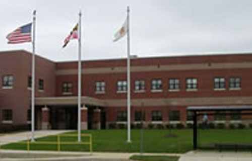 Three flags are flying in front of a brick building