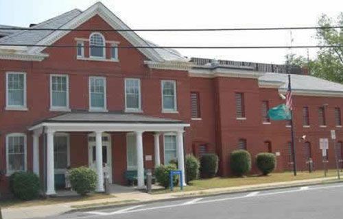 A large red brick building with a white porch on the side of the road.