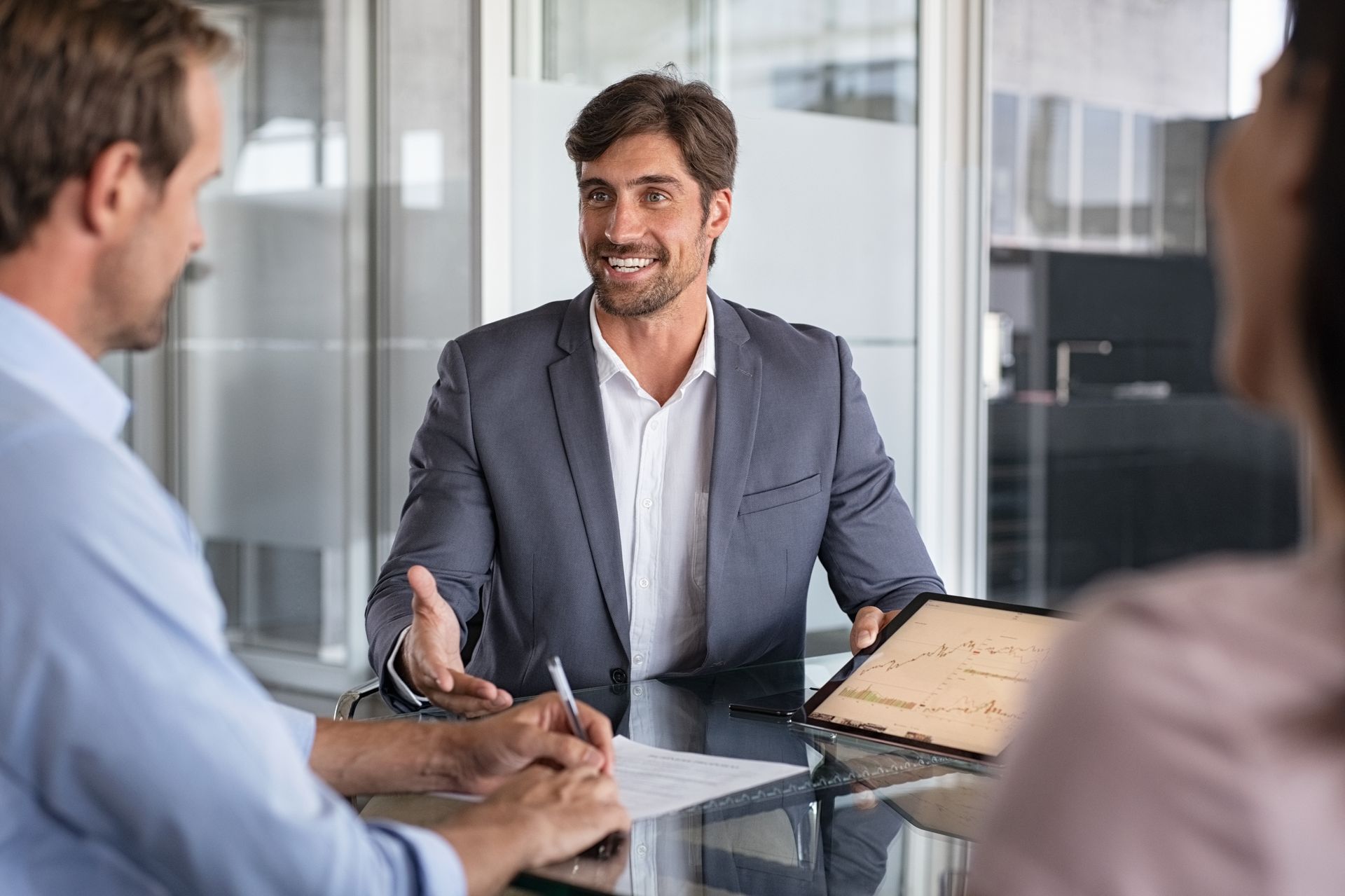 A man in a suit is sitting at a table talking to two people.