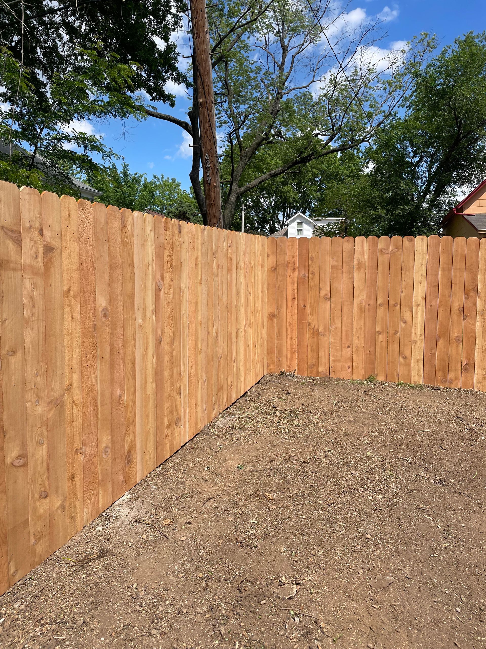 A wooden fence is surrounding a gravel area in a backyard.