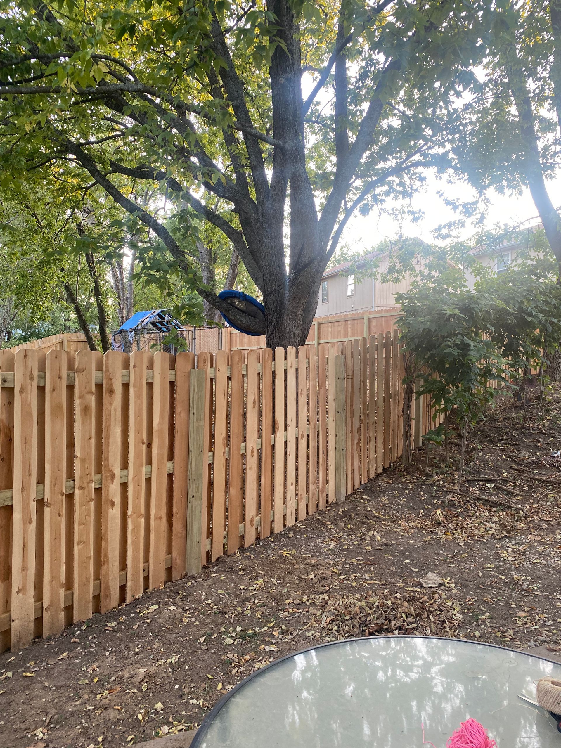 A wooden fence with a tree in the background and a table in the foreground.
