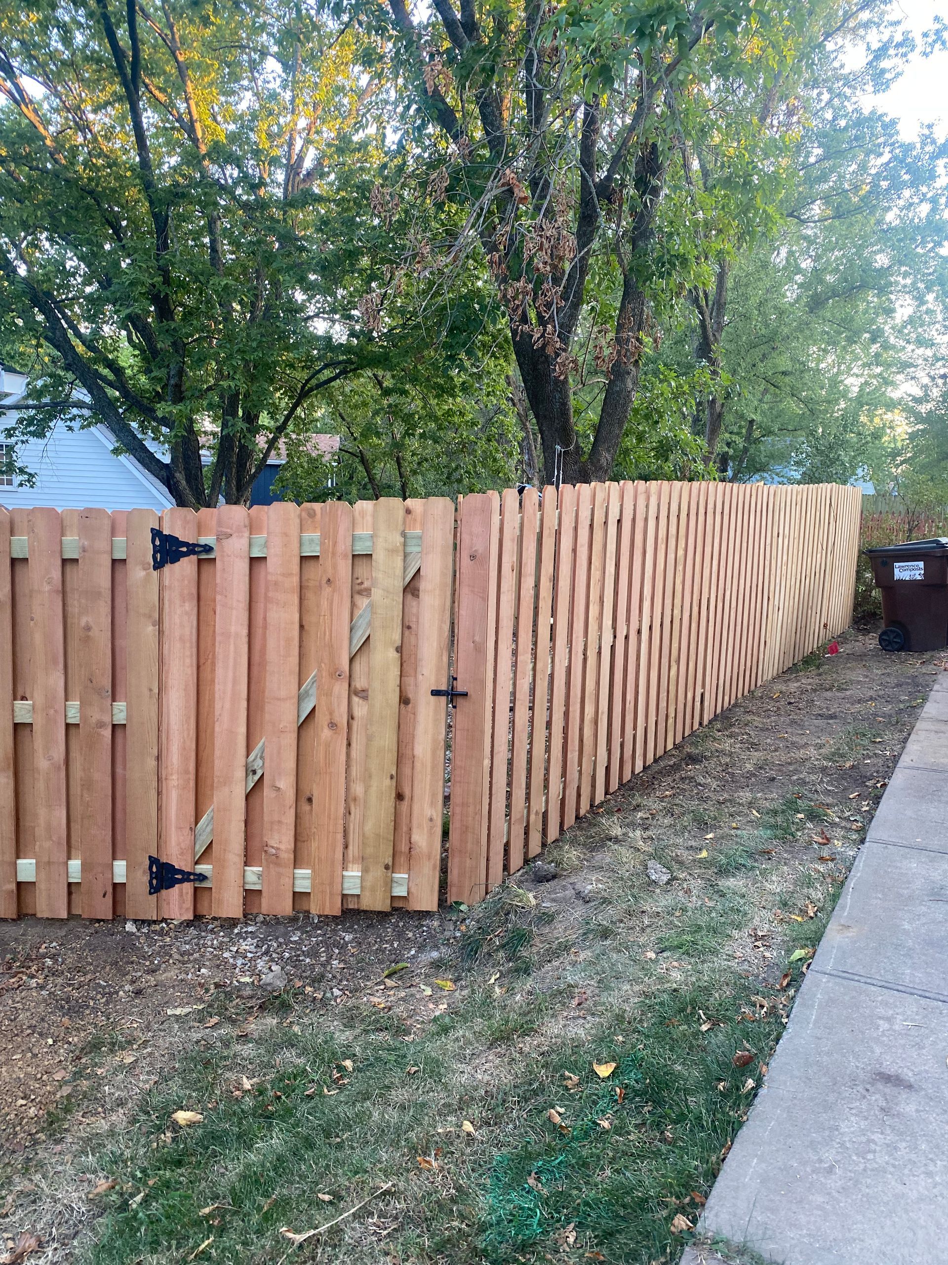 A wooden fence with a gate is sitting next to a sidewalk.