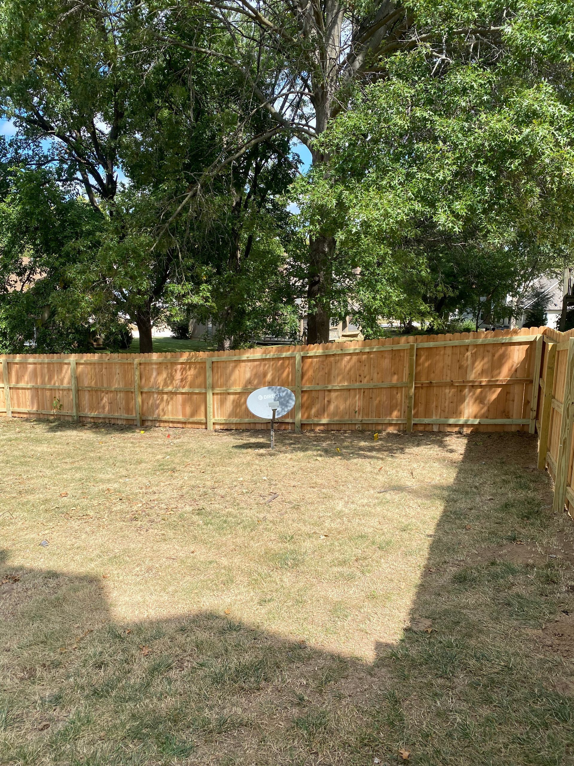A wooden fence with a satellite dish in the backyard.