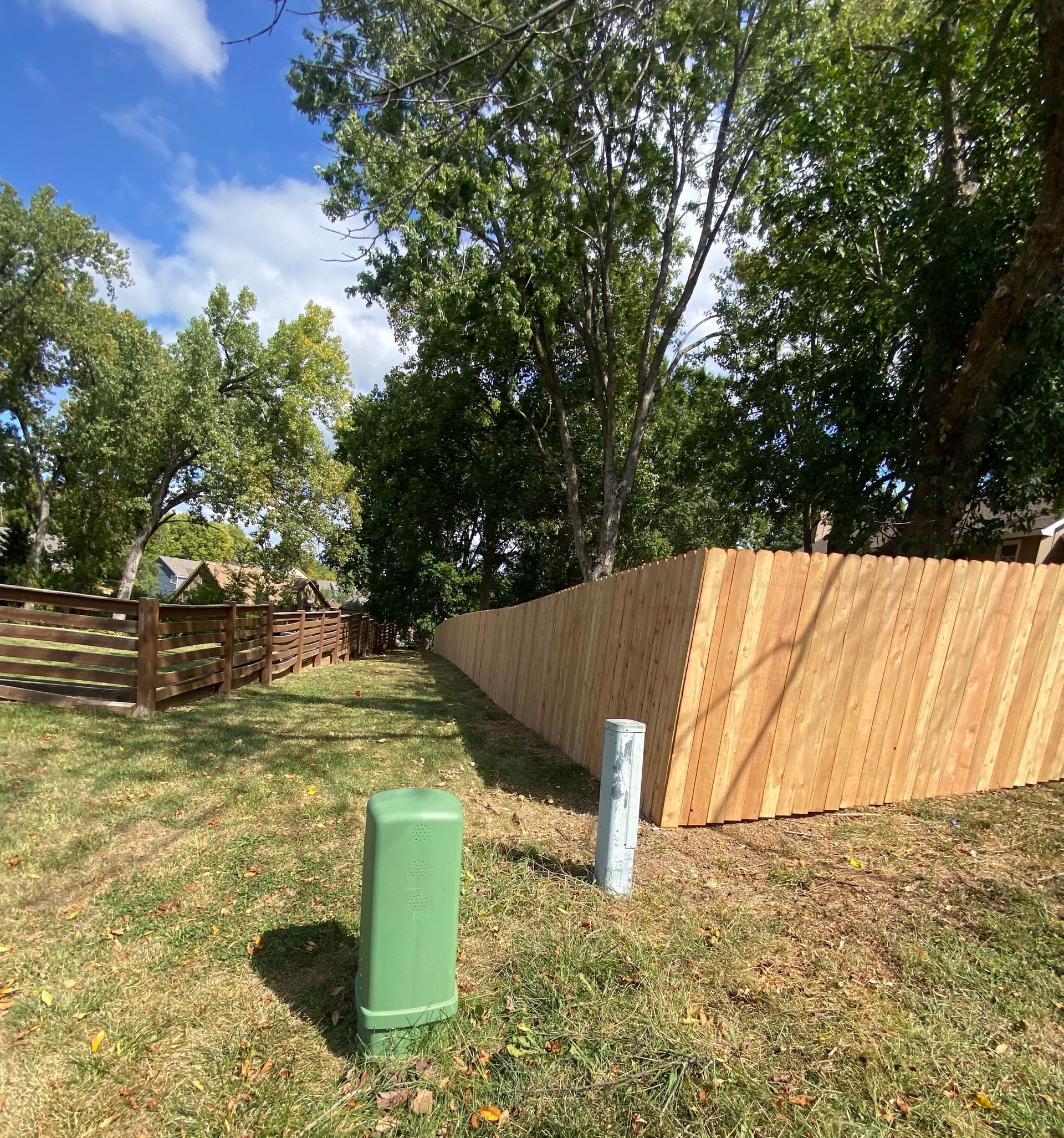 A wooden fence is surrounded by trees and grass in a yard.
