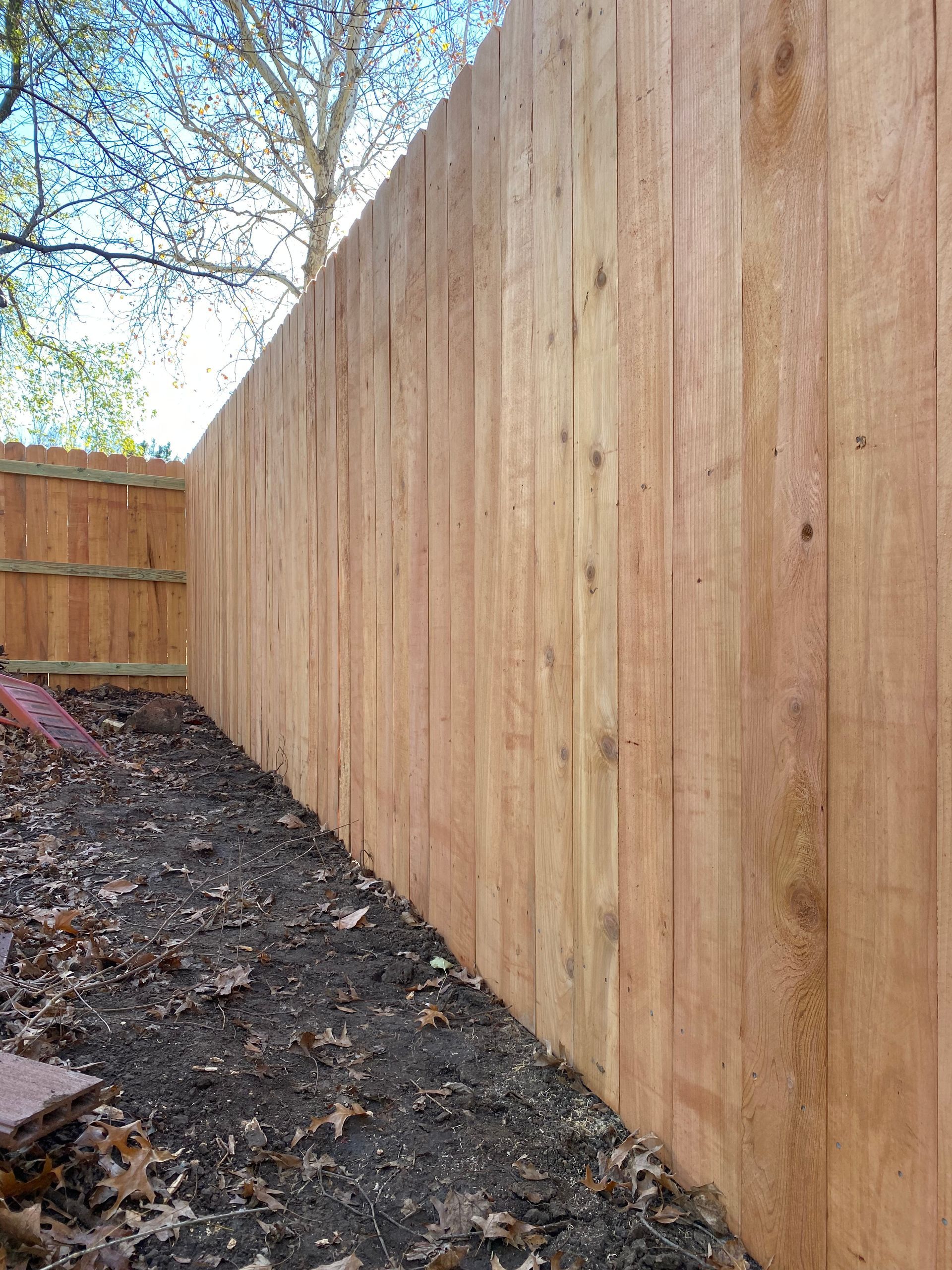 A wooden fence is surrounded by dirt and leaves in a backyard.